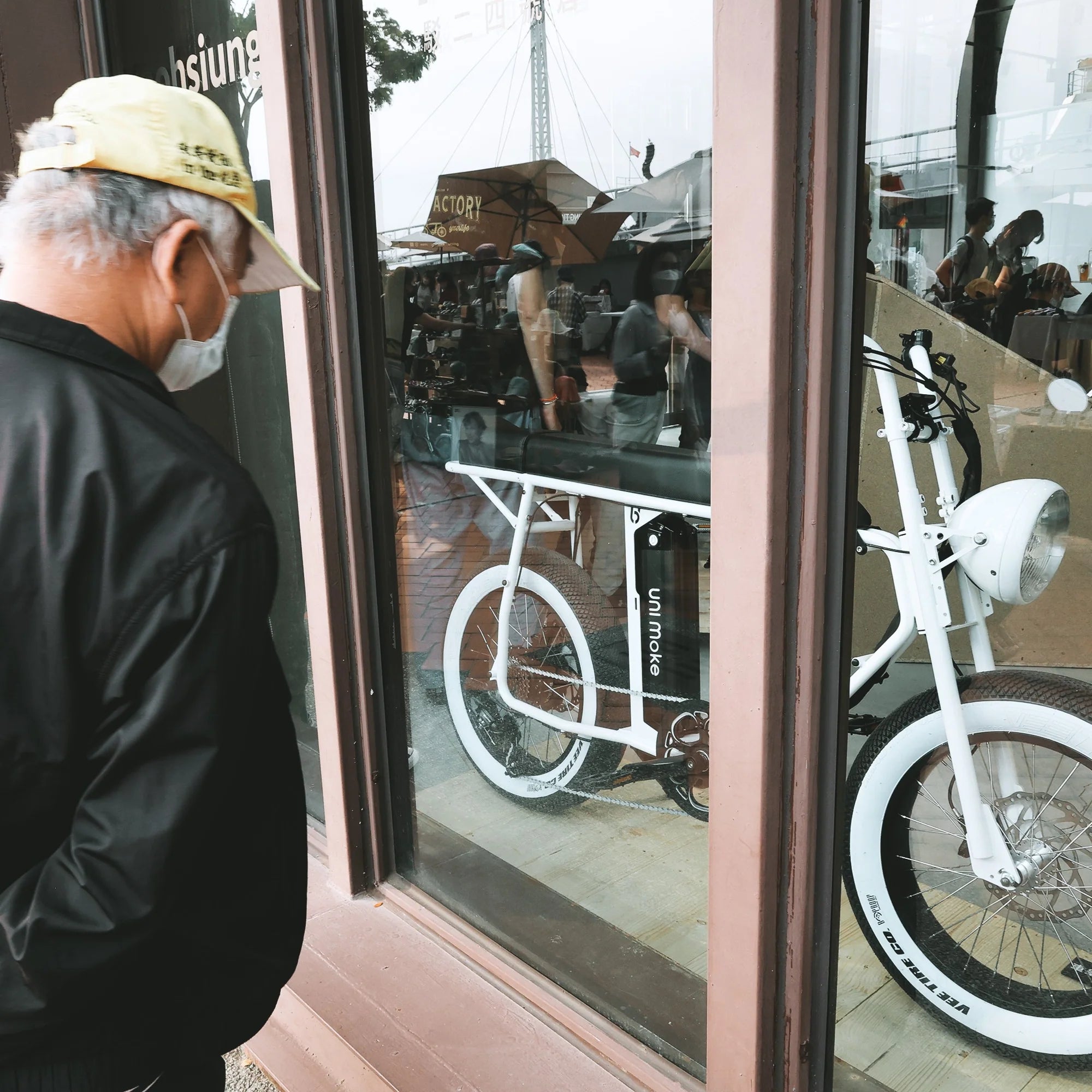 年長男性在 SEic 高雄駁二門市櫥窗前駐足,凝視展示中的白色 Unimoke 復古電輔車,展現跨越年齡層的工業美學吸引力