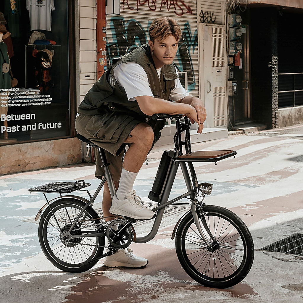 一個外國人在街頭跨坐在 SEic miniu 山貓石英灰上，車上安裝了前貨架及後貨架，時尚而實用