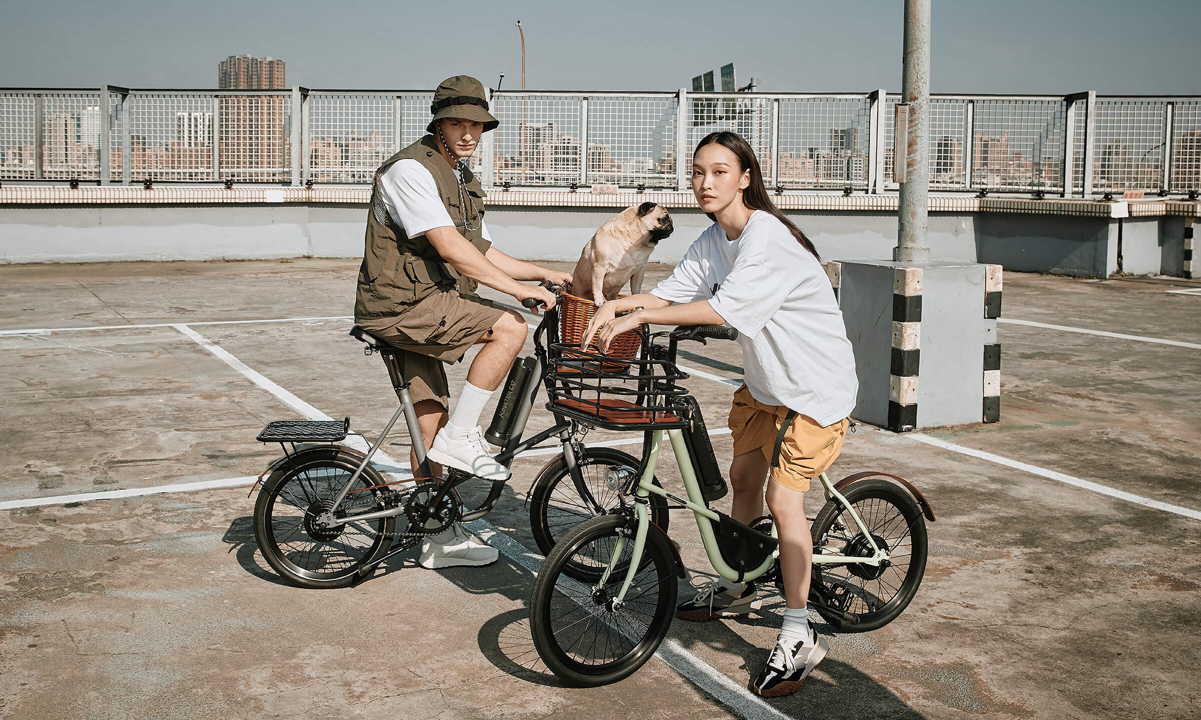 兩台低跨點輕電車，一台是灰色烤漆、另一台是綠色烤漆，場景在現代城市停車場頂樓，兩台都加裝了現代工業風cargo載物擴充配備，灰色車子的前貨籃上甚至還載了一支法鬥犬